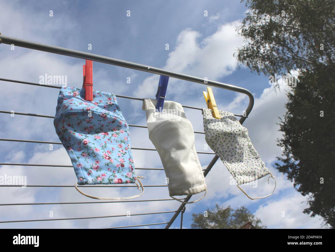 Trois masques faciaux en tissu réutilisables séchant sur une ligne de lavage à l'extérieur par temps ensoleillé. COVID 19 prévention, concept écologique. Banque D'Images