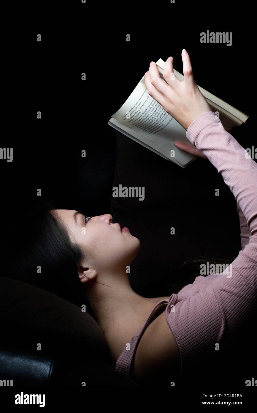 Une jeune femme mentait et lisant un livre la nuit Banque D'Images