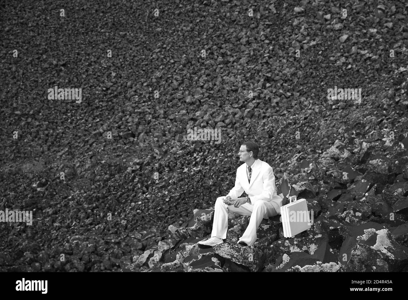 Homme d'affaires vêtu de blanc debout sur un fond sombre et sinistre de rochers. Banque D'Images