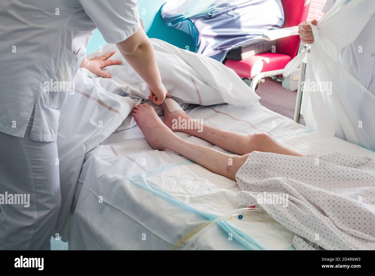Patient quadriplégique hospitalisé dans une salle PMR (personne à mobilité réduite), avec l'appui d'une infirmière et d'un soignant. Soins, prévention et surveillance Banque D'Images