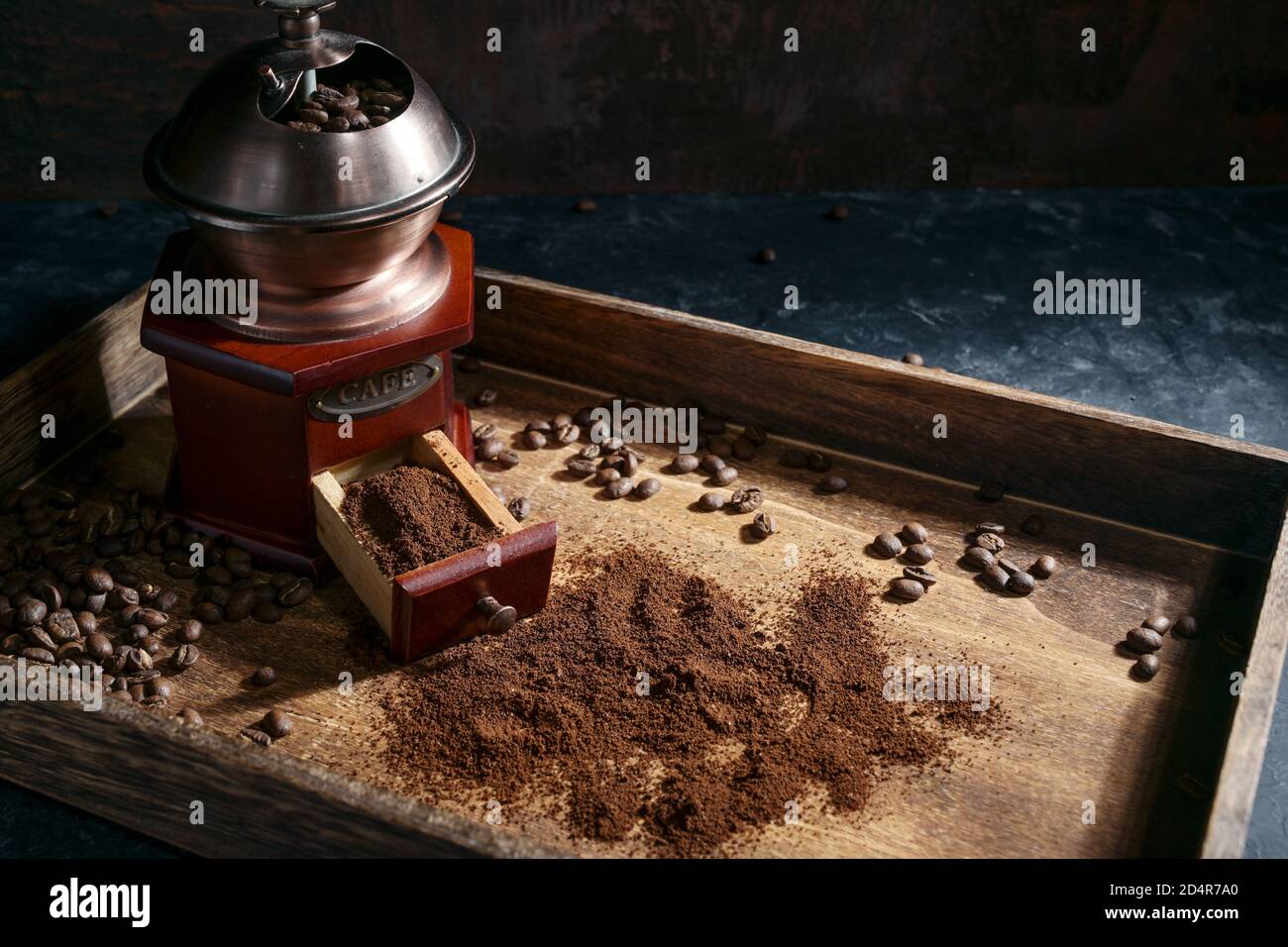 Moulin à café manuel nostalgique, grains torréfiés et café moulu sur plateau en bois rustique, fond sombre avec espace de copie, mise au point sélectionnée, petit rayon Banque D'Images