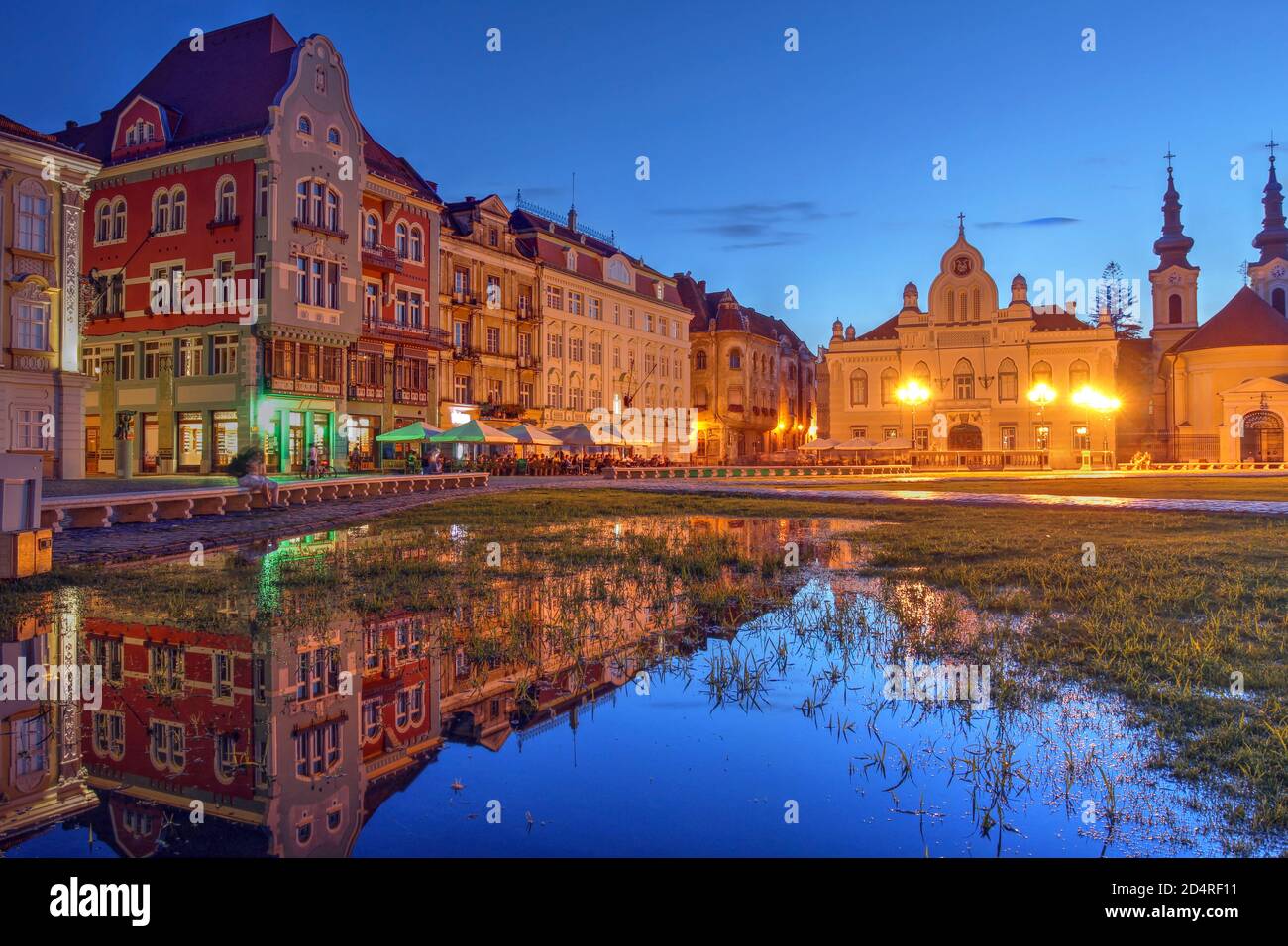 Scène nocturne sur la place Unirii (place Union), Timisoara, Roumanie avec une rangée de maisons historiques, se reflétant dans une piscine temporaire Banque D'Images