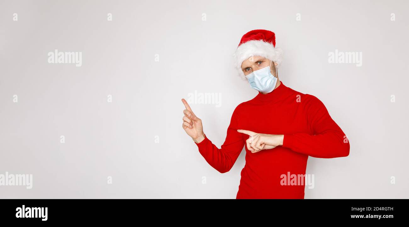 Noël pendant la pandémie du concept du coronavirus COVID-19. Bel homme portant un masque jetable et chapeau de père Noël. Modèle masculin avec chandail rouge Banque D'Images