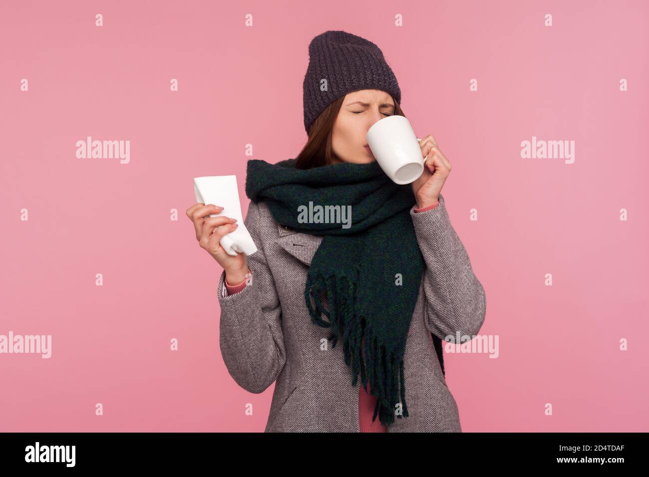 Une femme malsaine qui a la grippe boit une boisson médicale chaude pour se réchauffer, souffrant de virus ou de grippe saisonniers. Studio d'intérieur isolé sur le rose b Banque D'Images