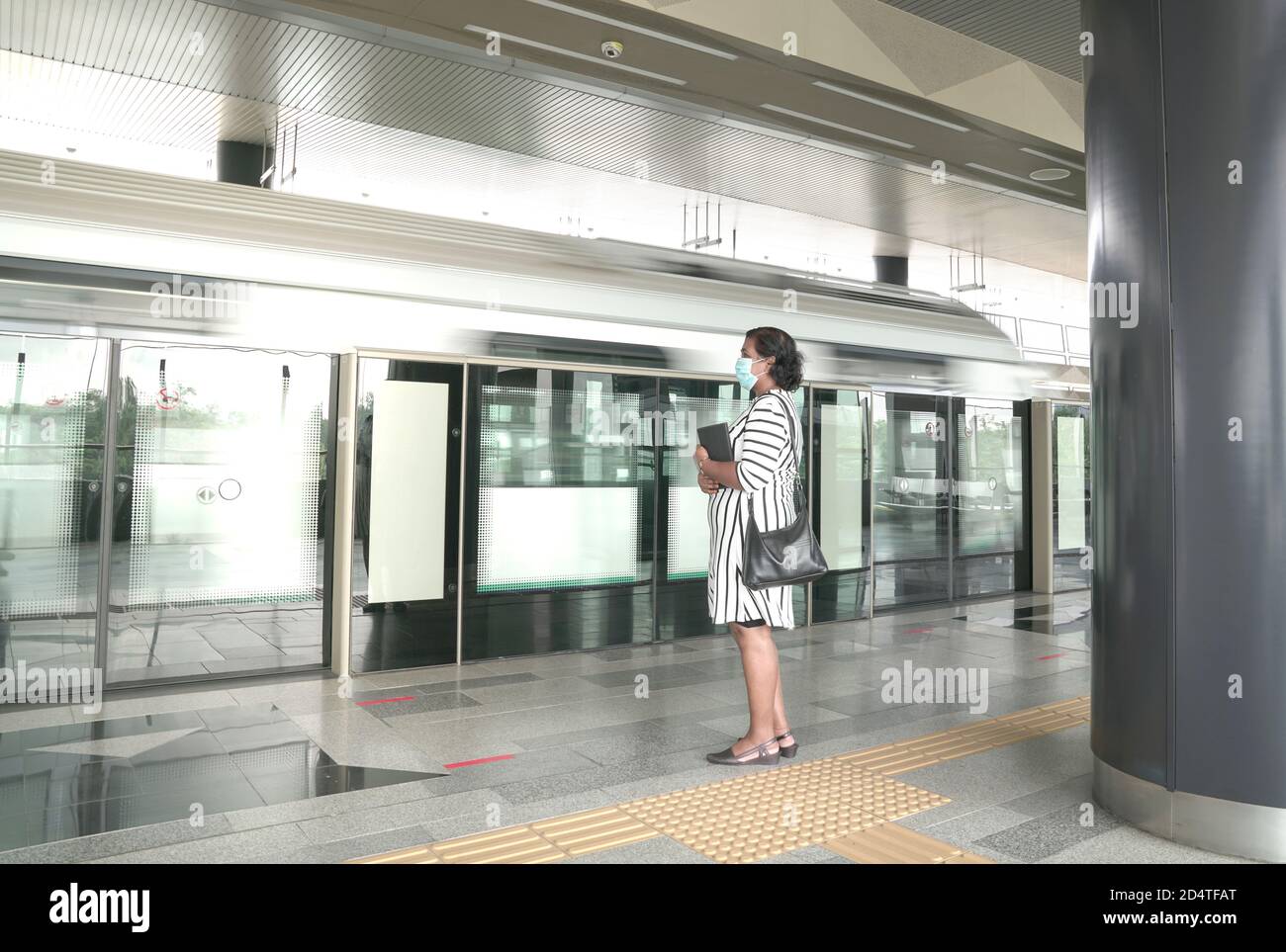 Femme portant un masque sur l'attente d'un train à la plate-forme d'une station de métro. Banque D'Images