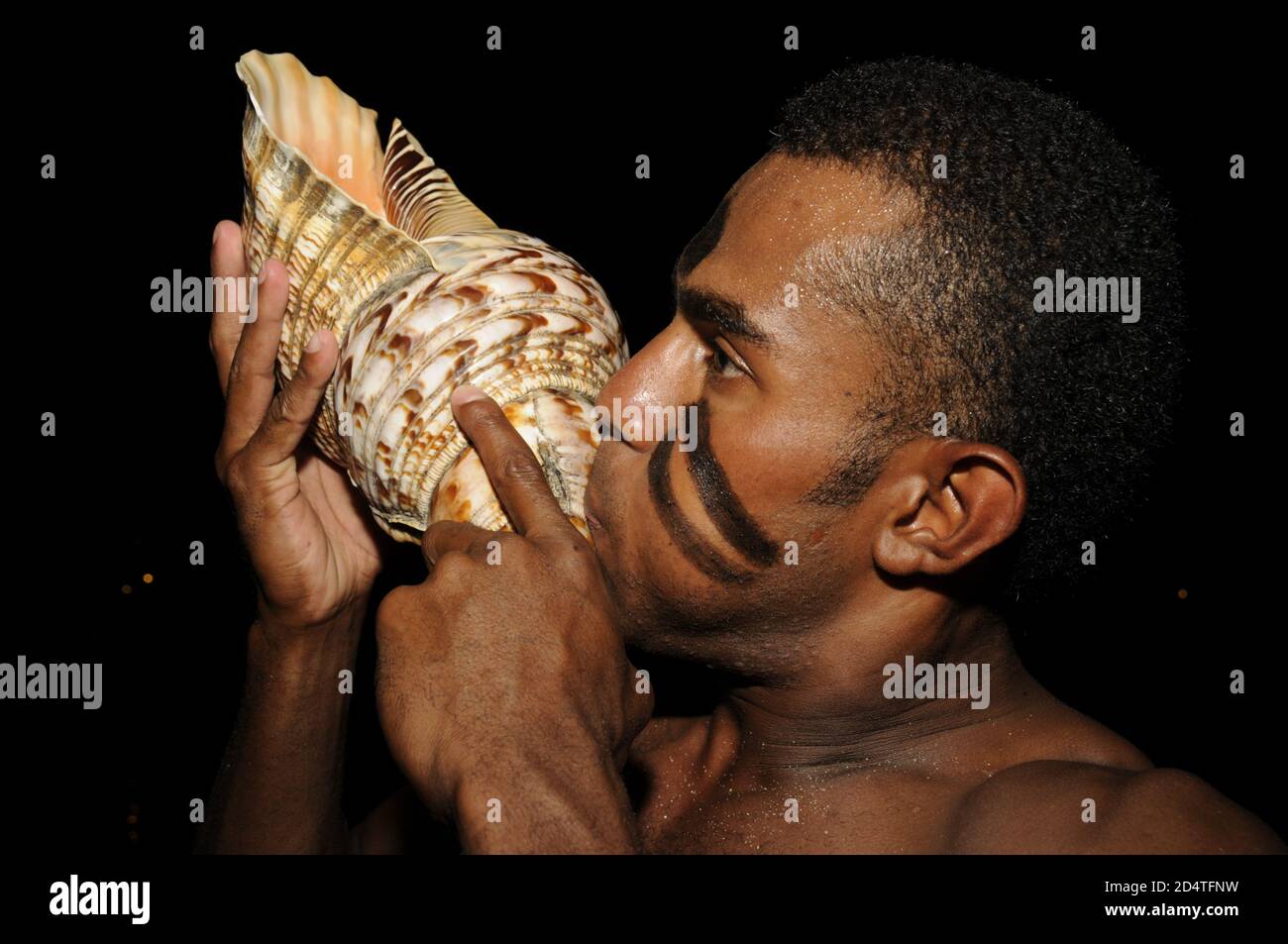 Un jeune Fijian souffle dans un seashell appelé un Davui. Il a été utilisé pour convoquer la communauté du village pour assister à une cérémonie à laquelle assistait le chef du village ou Banque D'Images