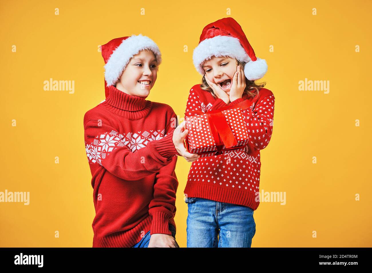 Happy boy in Santa hat boîte cadeau de Noël à excité Girl in red deer pullover sur fond jaune Banque D'Images