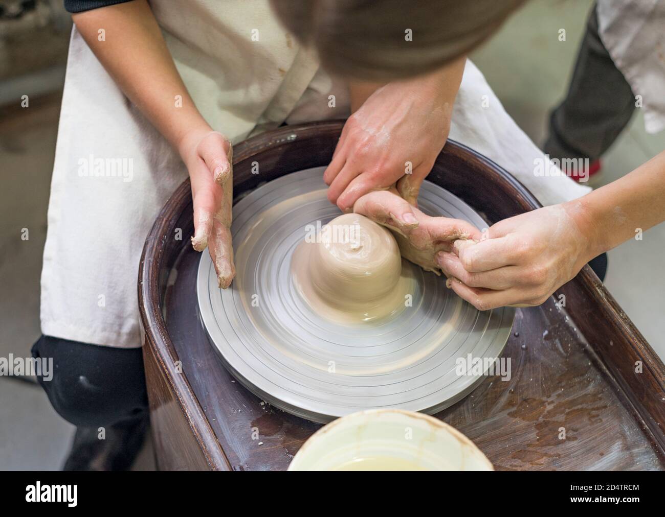 Un potier guide les mains d'un enfant pour l'aider à travailler avec la roue en céramique et l'argile. Gros plan de l'atelier. Apprentissage en cours. Banque D'Images