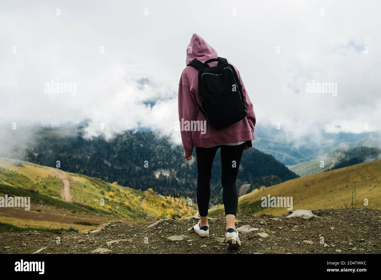 Femme décontractée dans des montagnes nuageux. Elle porte un sweat à capuche, un pantalon de yoga et un sac à dos Banque D'Images