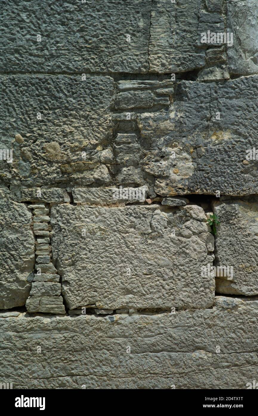 Vieux mur composé de différents types et tailles de pierres qui se sont détériorés et décolorés par le temps. Image d'arrière-plan Banque D'Images