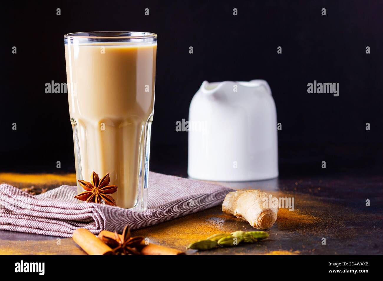 Verre de thé masala et épices éparses. Masala chai thé et pot à lait sur fond noir. Copier l'espace Banque D'Images