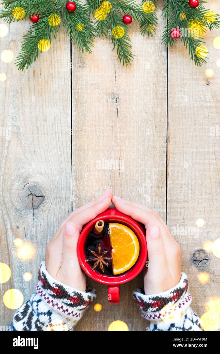 Mains tenant une tasse en céramique rouge avec du vin chaud, fond en bois avec espace de copie. Banque D'Images