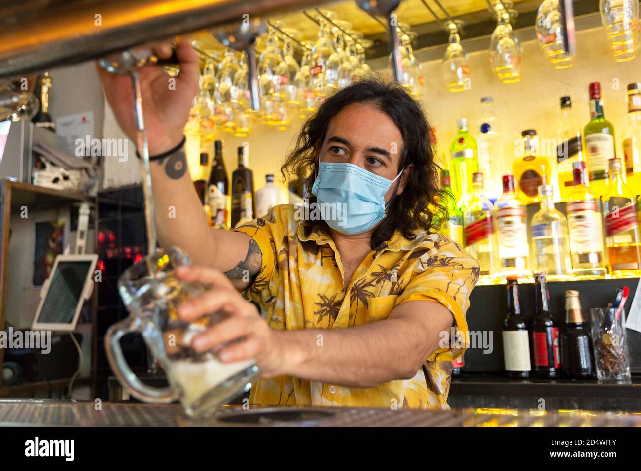 Vue de face d'un serveur qui verse un pichet de bière dans un bar. Il porte un masque médical. Banque D'Images