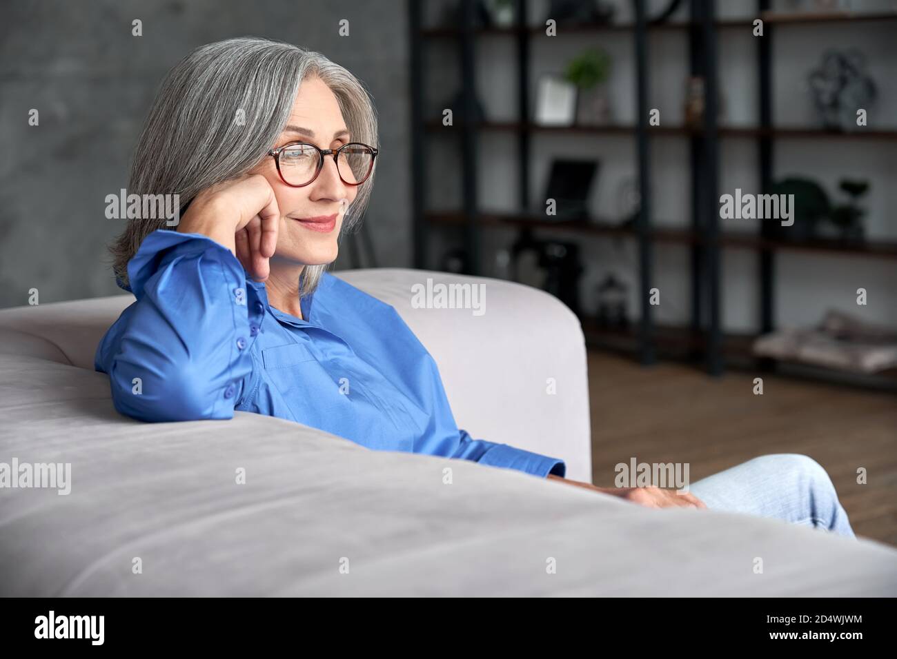 Belle femme mûre et âgée portant des lunettes se détendant sur un canapé à la maison. Banque D'Images