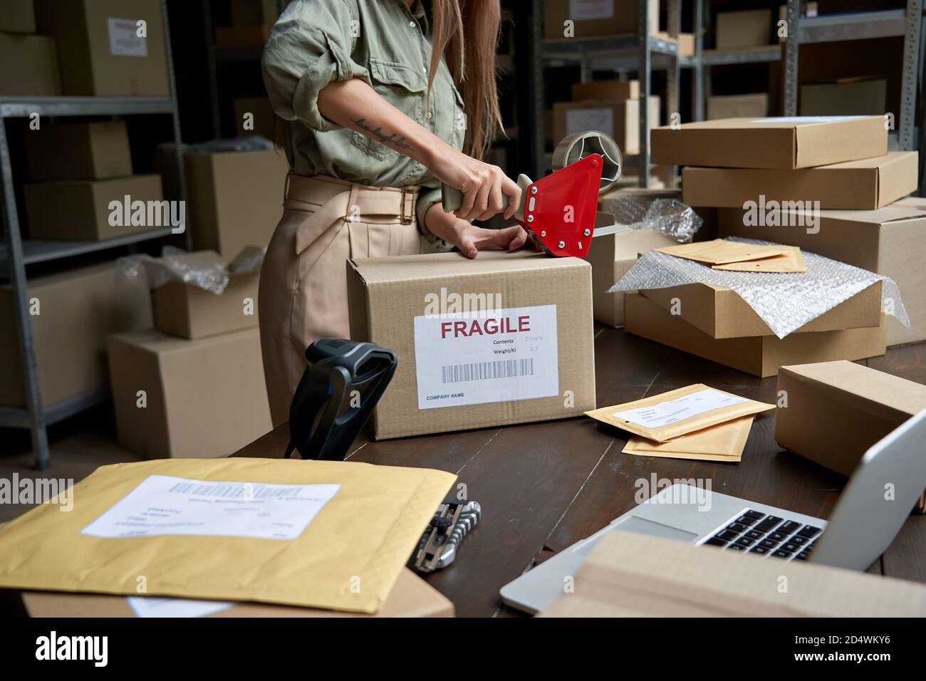 Une employée de post-mail qui tient le distributeur de ruban adhésif dans la boîte d'expédition. Banque D'Images
