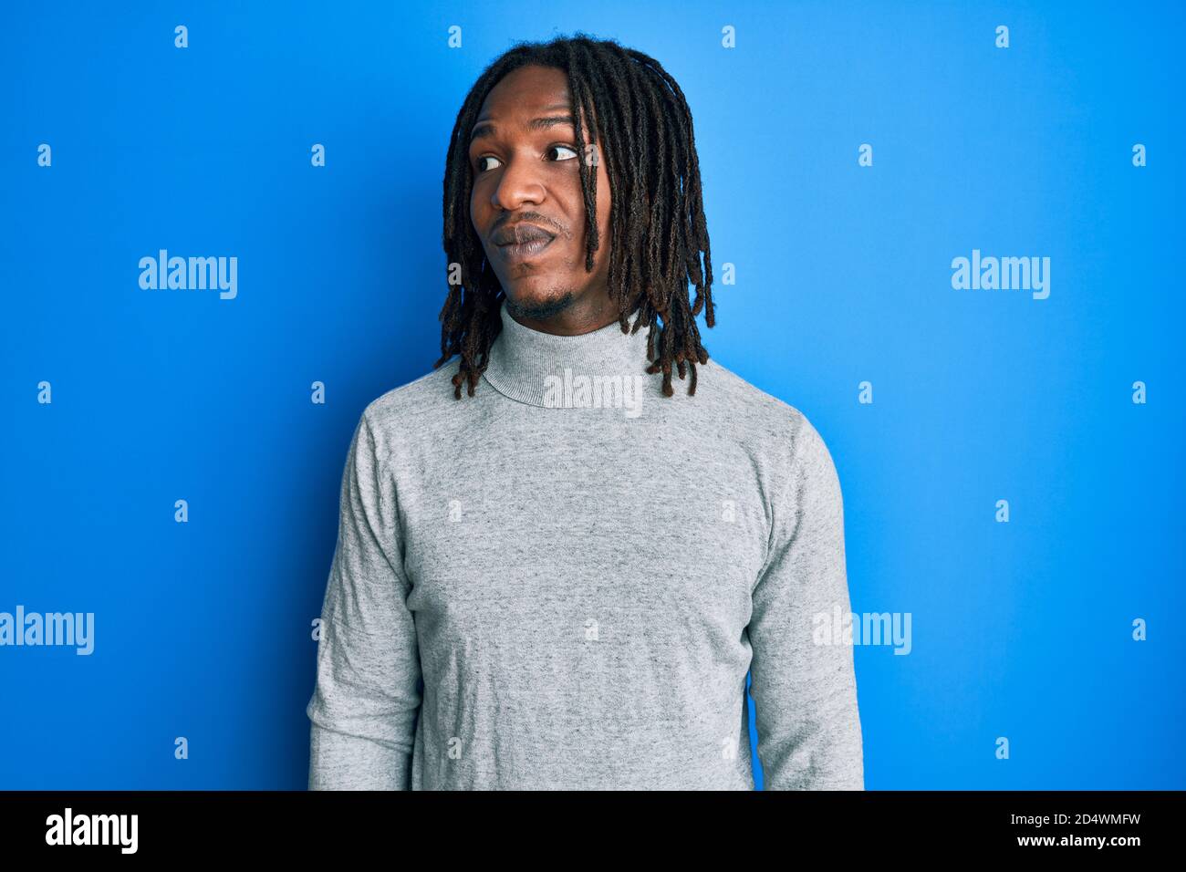 Homme afro-américain avec des tresses portant un pull à col roulé souriant  à côté et regardant loin de penser Photo Stock - Alamy