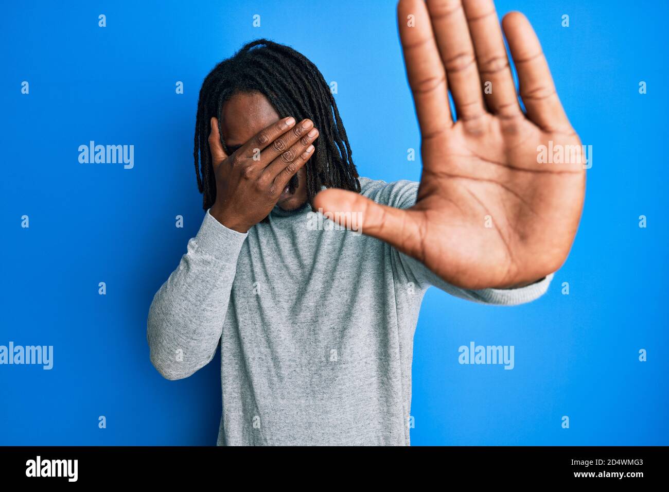 africain américain homme avec des tresses portant un pull à col roulé  couvrant les yeux avec les mains et faisant un geste d'arrêt avec  l'expression triste et de peur. Embarrassé Photo Stock -