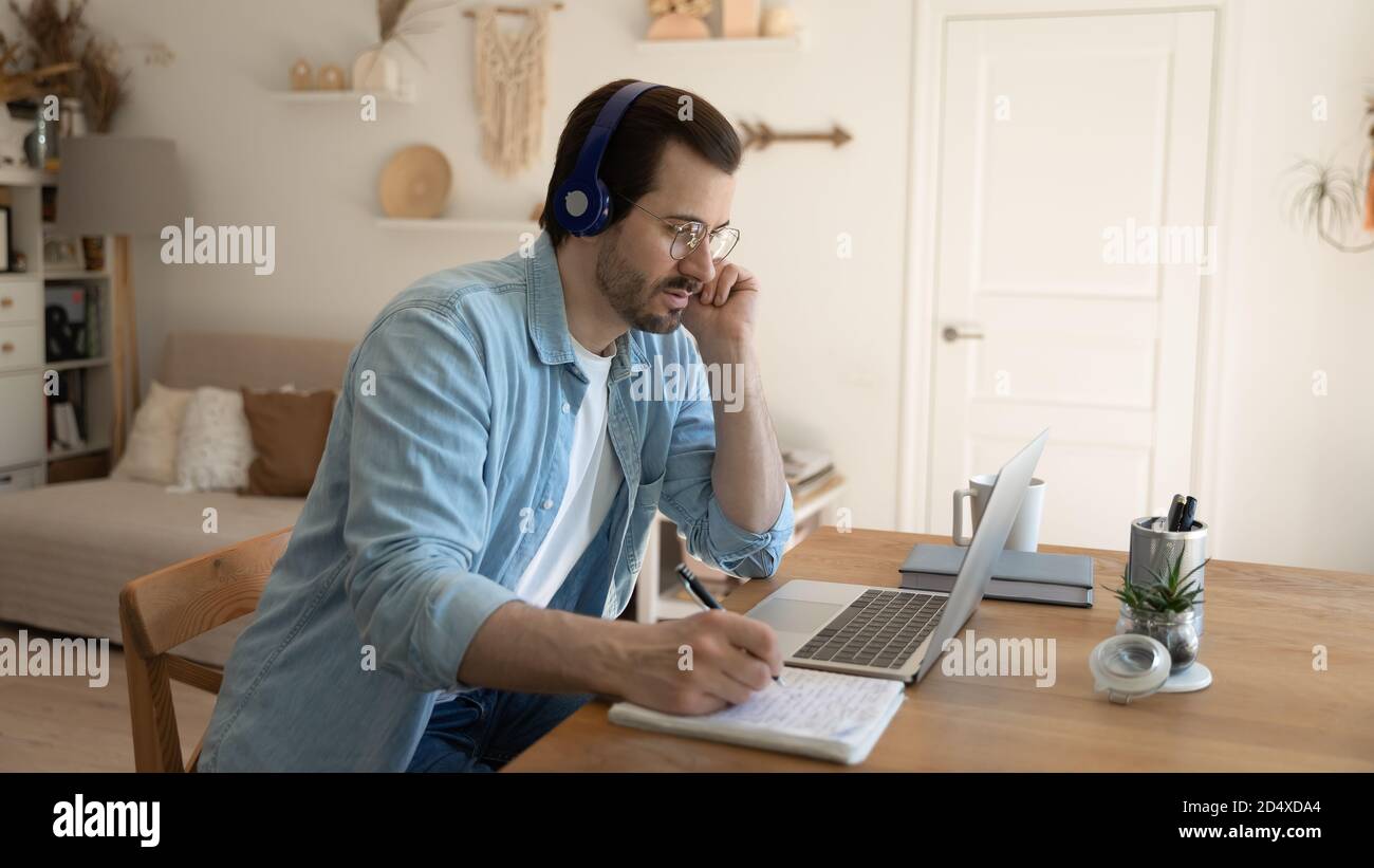 Jeune homme concentré étudiant sur des cours en ligne au bureau à domicile. Banque D'Images