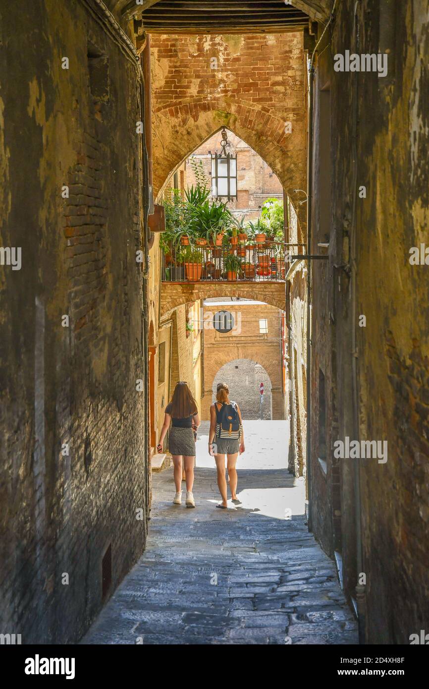 Deux filles marchant à Vicolo delle Scotte, une ruelle médiévale étroite dans le ghetto juif de Sienne, site du patrimoine mondial de l'UNESCO, Toscane, Italie Banque D'Images