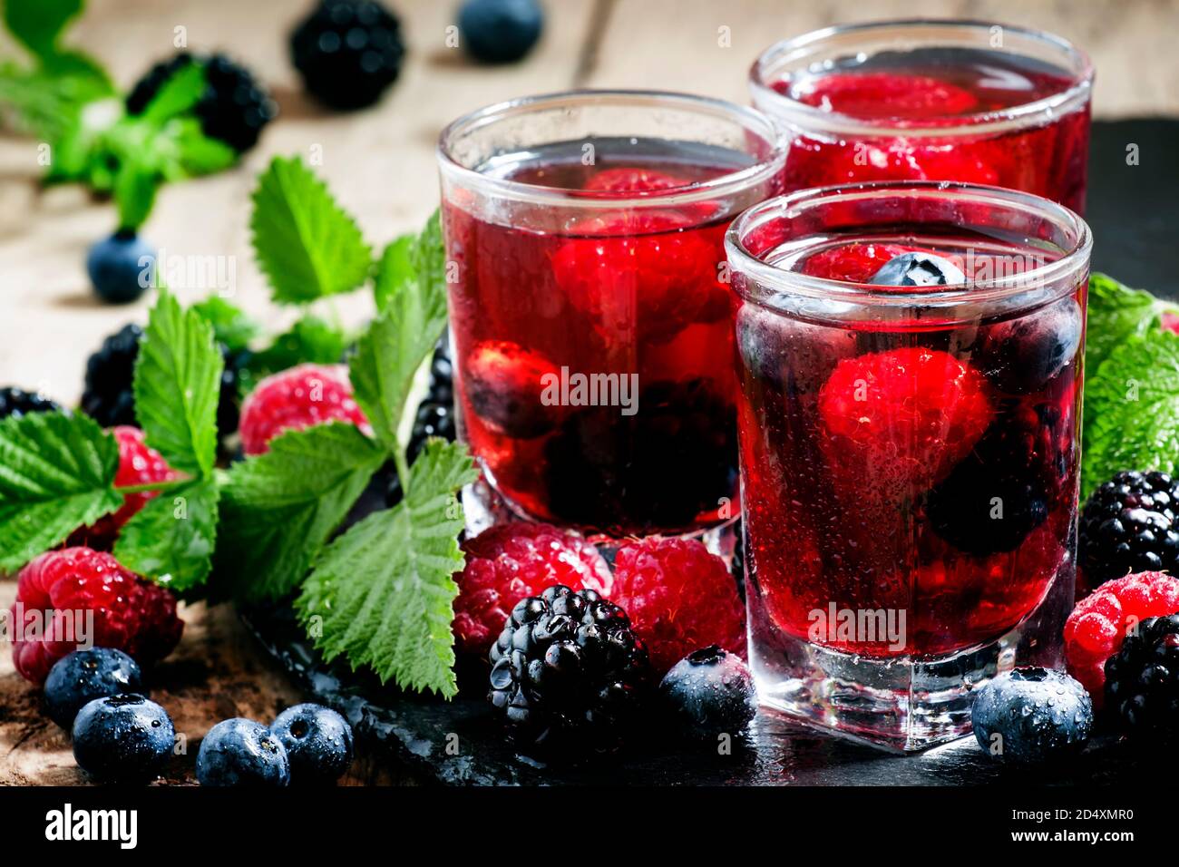 Thé froid aux baies d'été avec framboises, bleuets, mûres et menthe dans des verres embués sur un fond sombre, foyer sélectif Banque D'Images