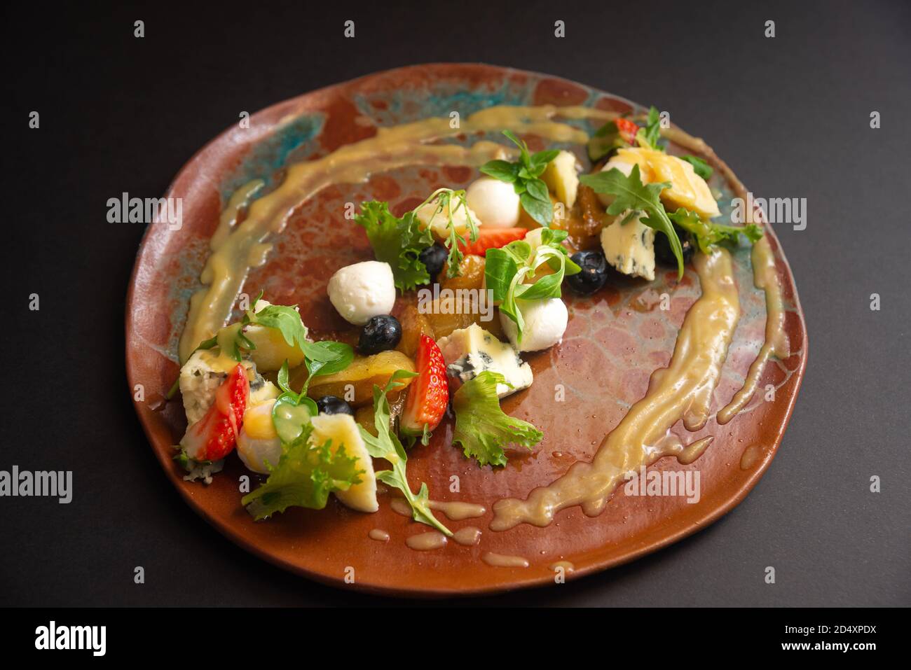 Salade de fromage et de fruits sur une assiette faite à la main. Mozzarella, fromage bleu, parmesan, rouleaux de courgettes, micro verts, bleuets, quartiers de fraises Banque D'Images
