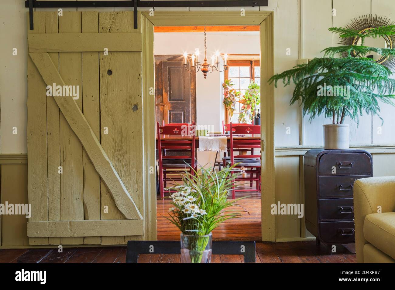 Porte de grange coulissante en bois menant à la salle à manger du salon  avec vase de fleur sur table basse à l'intérieur d'une ancienne maison en  pierre de style cottage de
