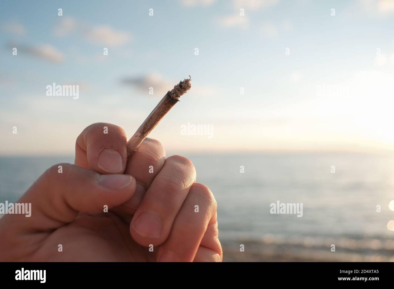 Main humaine tenir une cigarette de tabac sur la mer du coucher du soleil contexte,problème de dépendance au tabagisme Banque D'Images