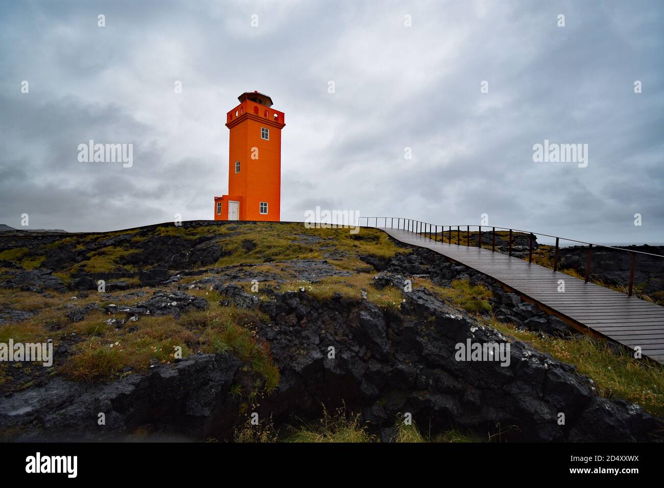 Un sentier mène au phare orange de Svortuloft sur la péninsule de Snaefellsnes, dans l'ouest de l'Islande. Le phare est situé sur une roche de lave noire. Banque D'Images