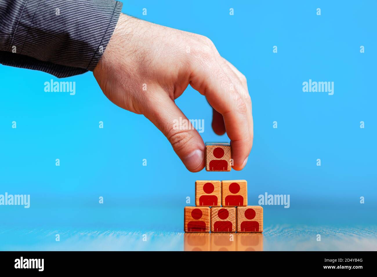Gestion des ressources humaines et concept d'entreprise de recrutement. Placer à la main le bloc cube en bois sur la pyramide supérieure. Copier l'espace. Arrière-plan bleu. Banque D'Images