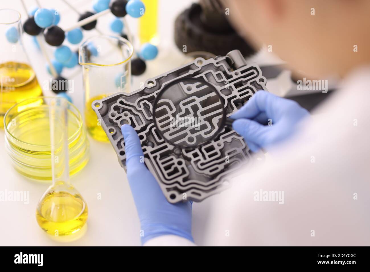 Les mains dans les gants en caoutchouc tiennent la loupe sur la boîte de vitesses automatique en laboratoire Banque D'Images