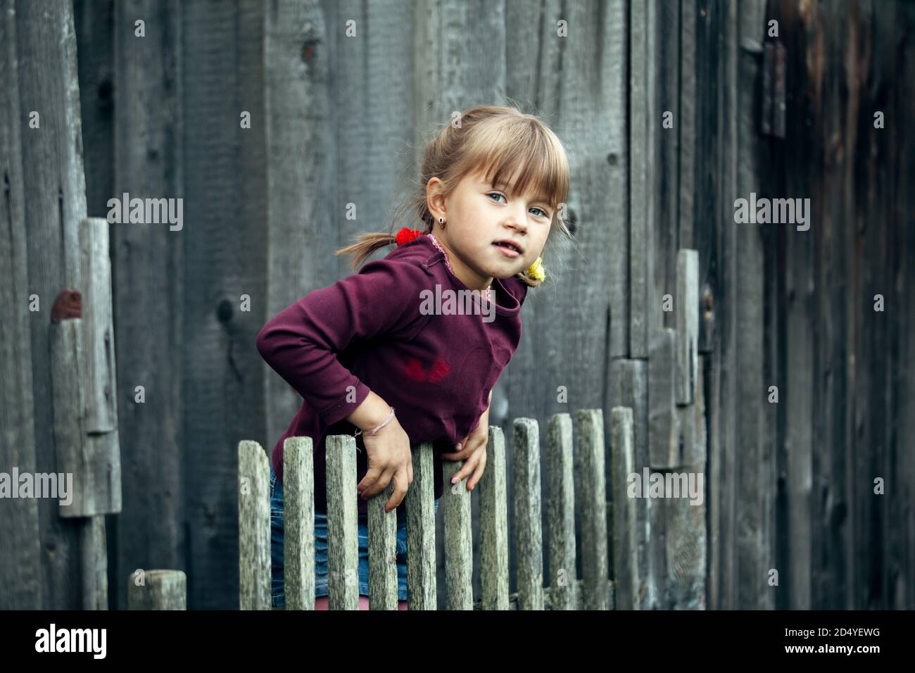 Petite petite jolie fille drôle près de la clôture rurale vintage. Banque D'Images