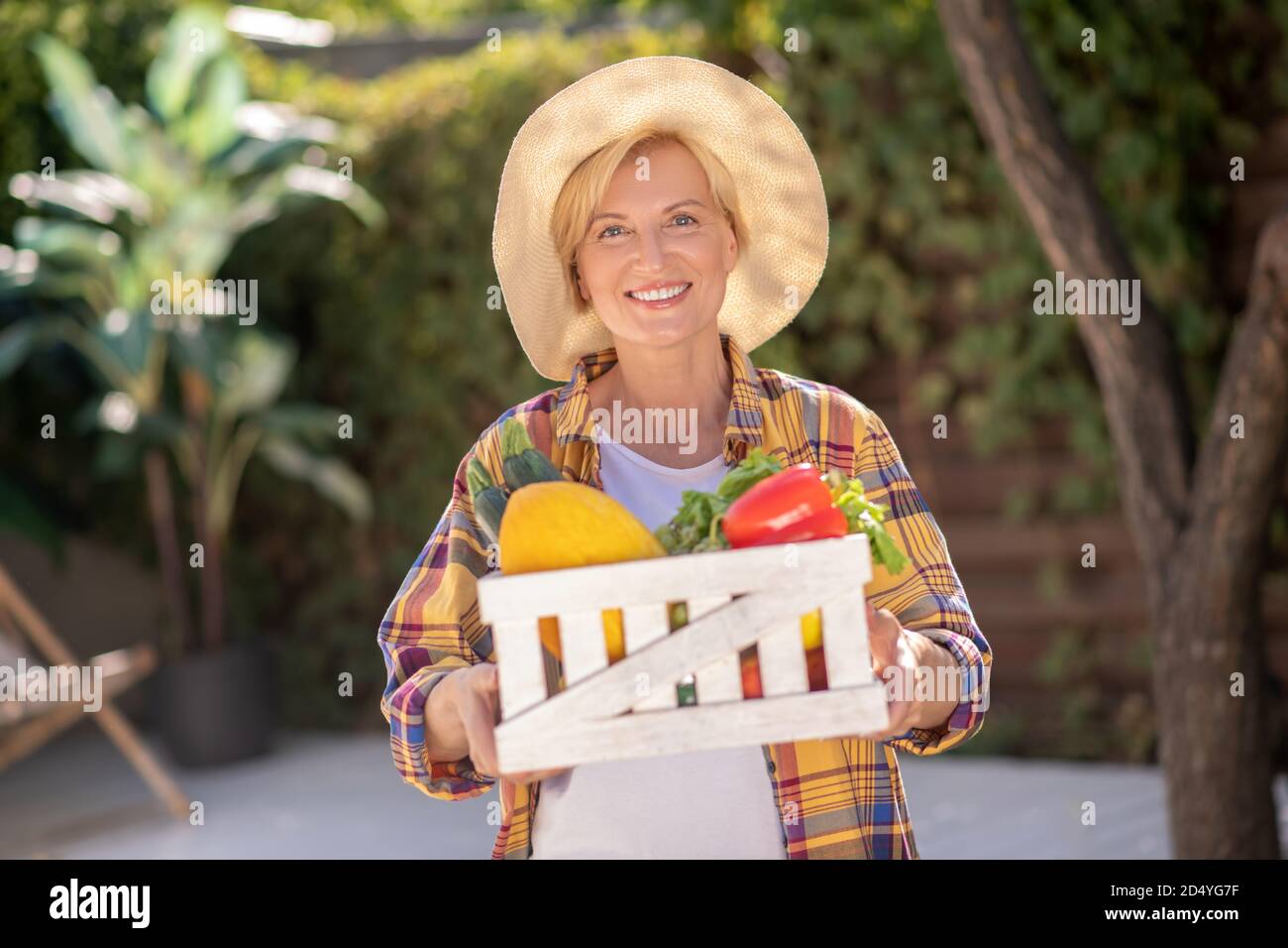 Femme blonde souriante en chapeau de paille tenant le panier avec les légumes Banque D'Images