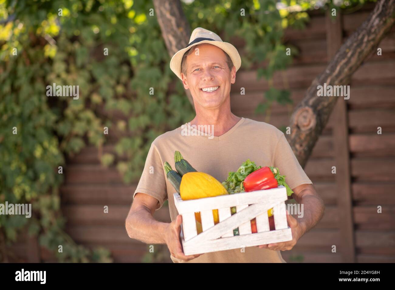 Homme souriant dans un chapeau de paille tenant le panier avec les légumes Banque D'Images