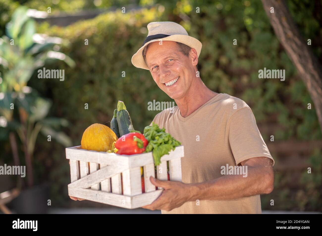 Joyeux homme en chapeau de paille tenant le panier avec les légumes Banque D'Images