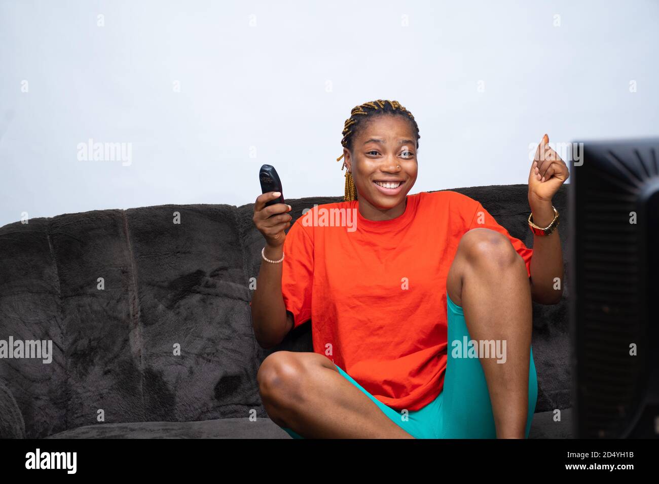 Une femme africaine excitée se réjouit de regarder la télévision à la maison, en tenant la télécommande du téléviseur Banque D'Images
