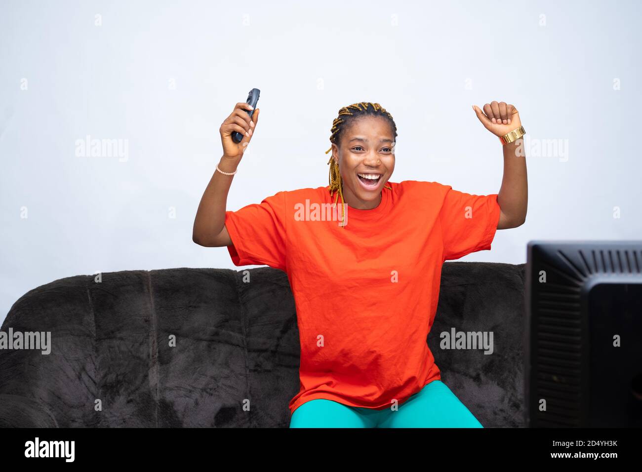 Une femme africaine se réjouit de regarder la télévision à la maison, tenant la télécommande du téléviseur, applaudissait son équipe ou son joueur Banque D'Images