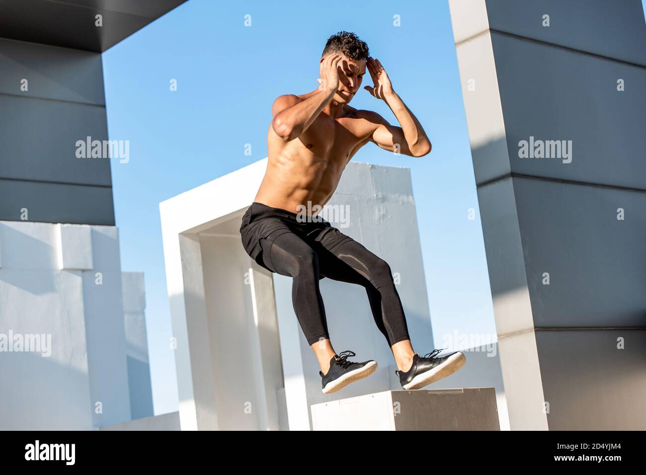 FIT shirless homme de sport sautant jusqu'à la boîte en bois plyométrique à l'extérieur sur le toit du bâtiment, à la maison musculation exercice concept Banque D'Images