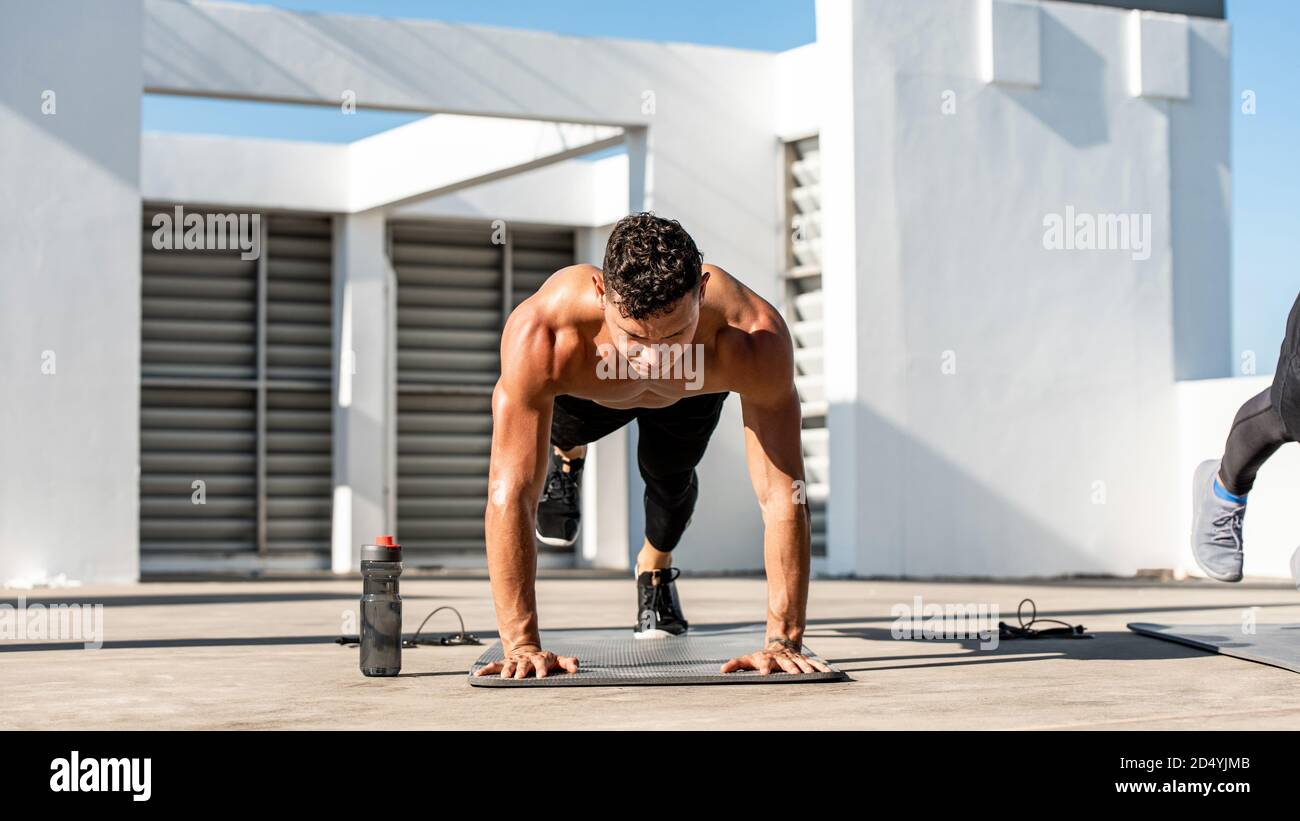 Athlète masculin sans chirless musclé faisant un exercice de levage de jambe de planche haute en plein air sur le toit du bâtiment Banque D'Images