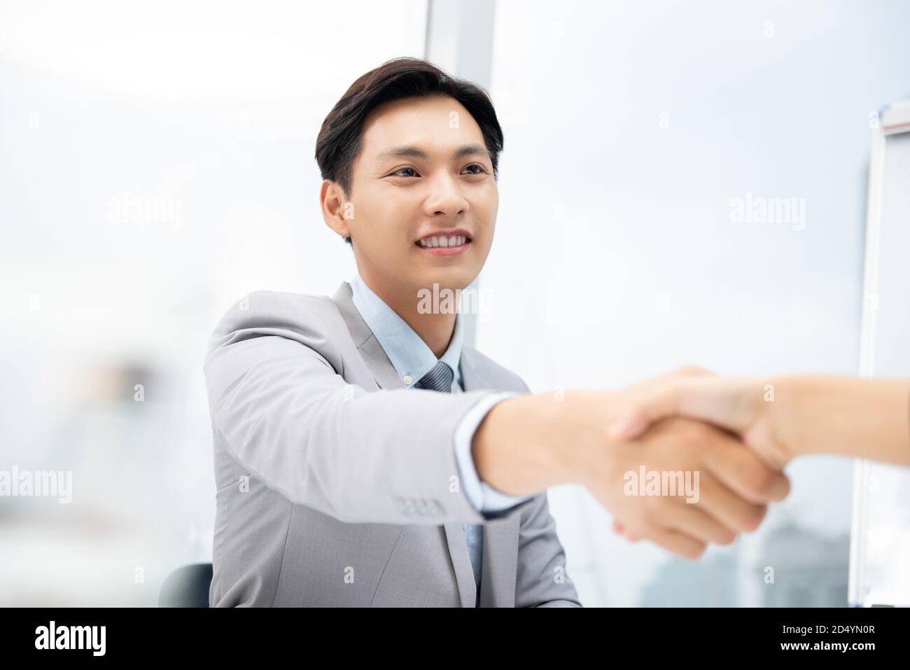 Jeune homme d'affaires asiatique amical souriant et faisant poignée de main avec son partenaire au bureau Banque D'Images