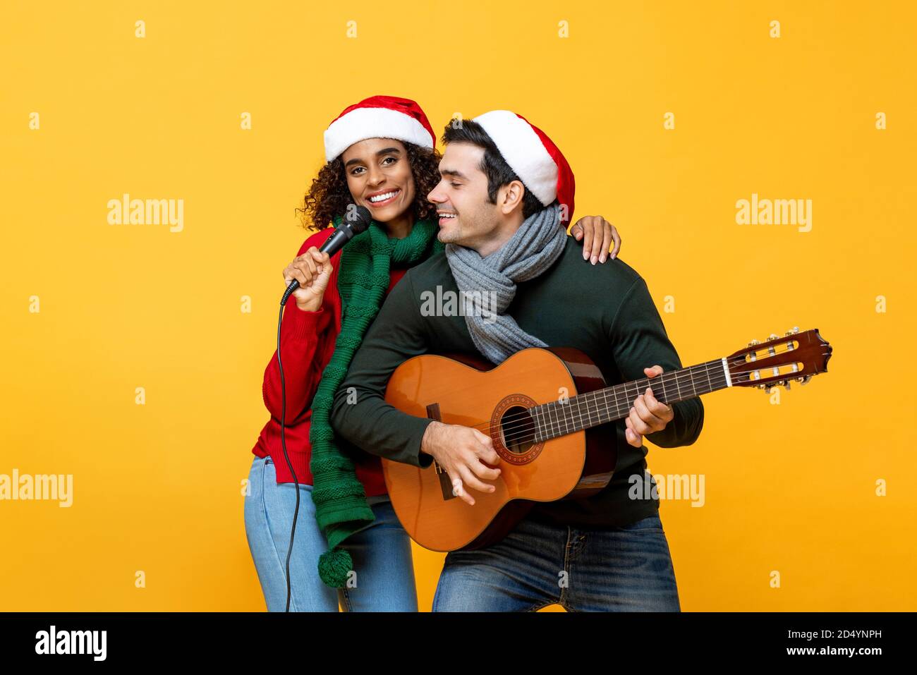 Heureux couple interracial chantant une chanson célébrant Noël dans isolé fond de studio jaune Banque D'Images