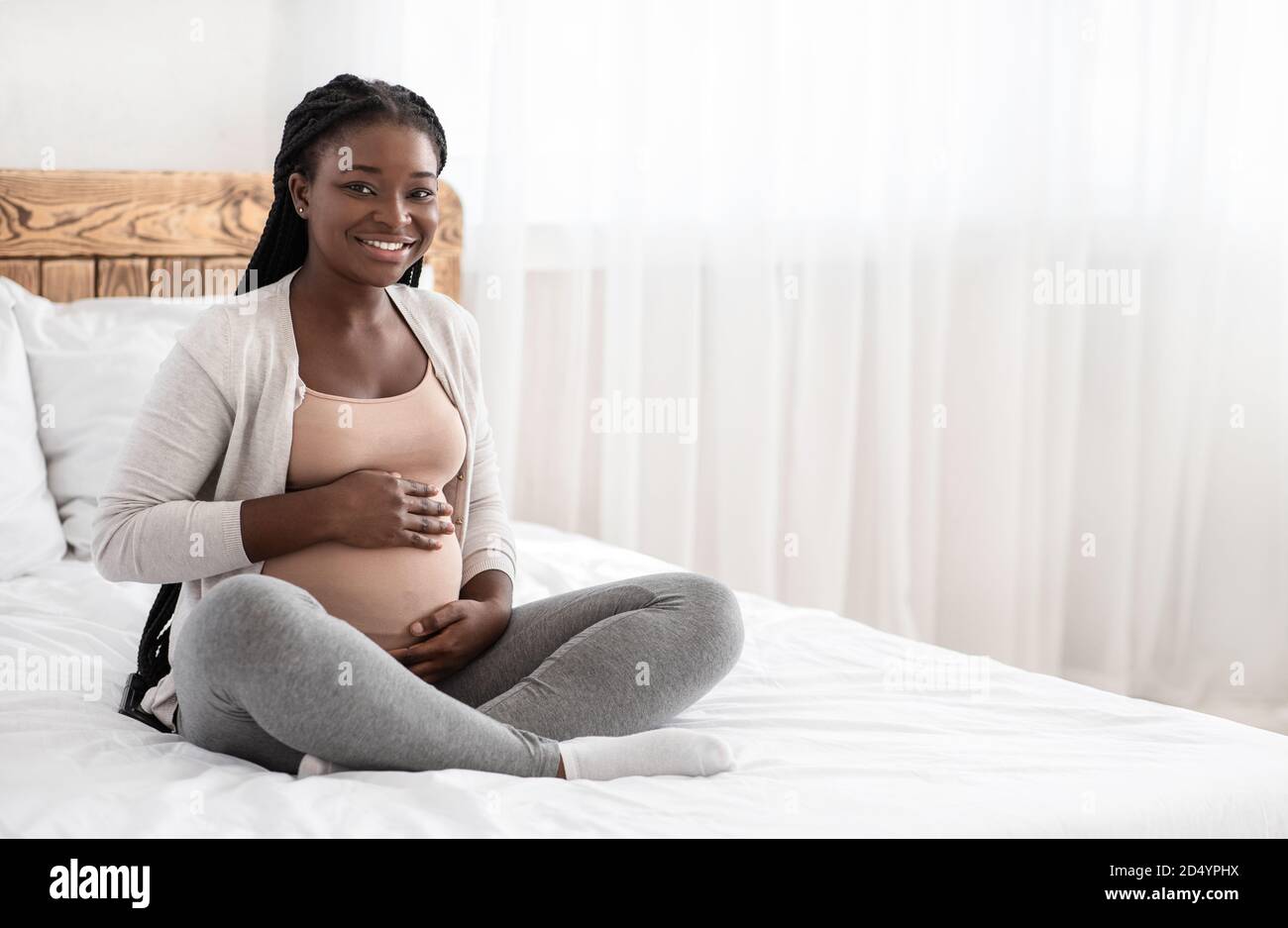 Temps de grossesse. Bonne femme enceinte noire assise sur le lit touchant Belly Banque D'Images
