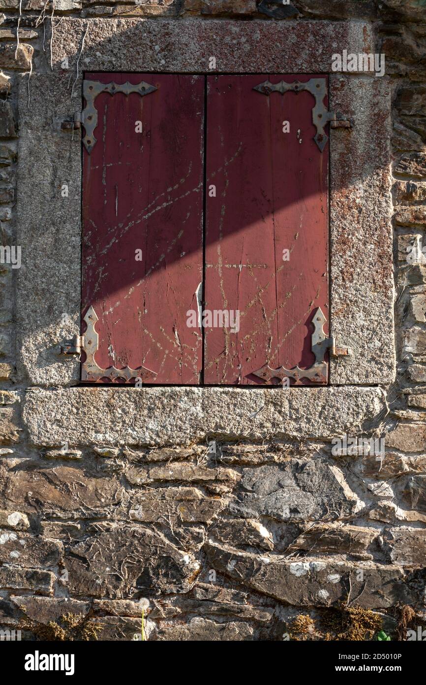 Fenêtre espagnole en bois rouge avec volets et cadre en pierre. Construction architecture maison de campagne rustiques en pierre. Banque D'Images