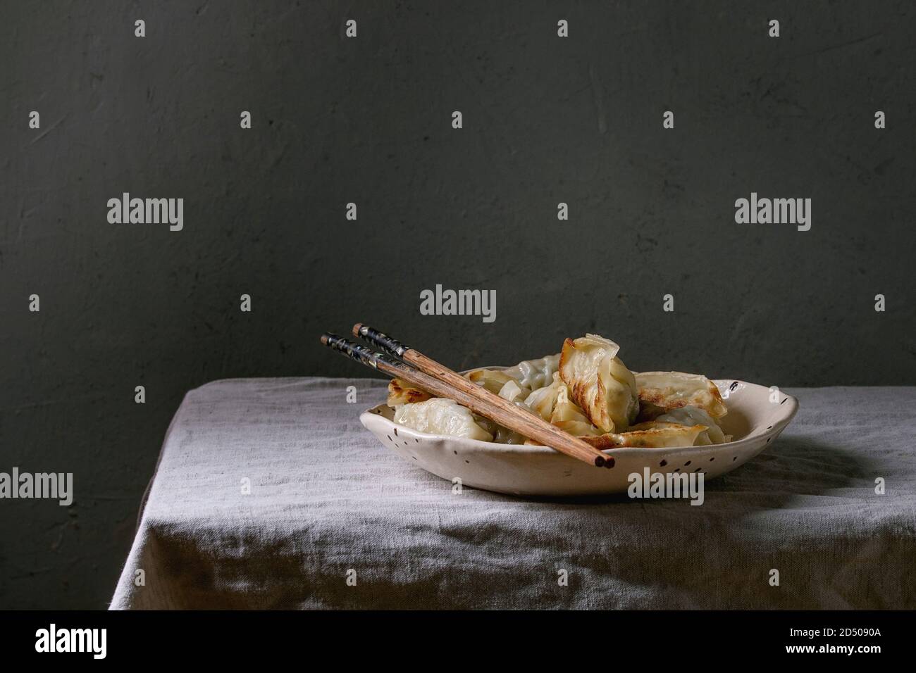 Les Gyozas frits boulettes asiatiques potstickers dans une plaque en céramique blanc servi avec des baguettes plus , tapis de table. Dîner asiatique Banque D'Images