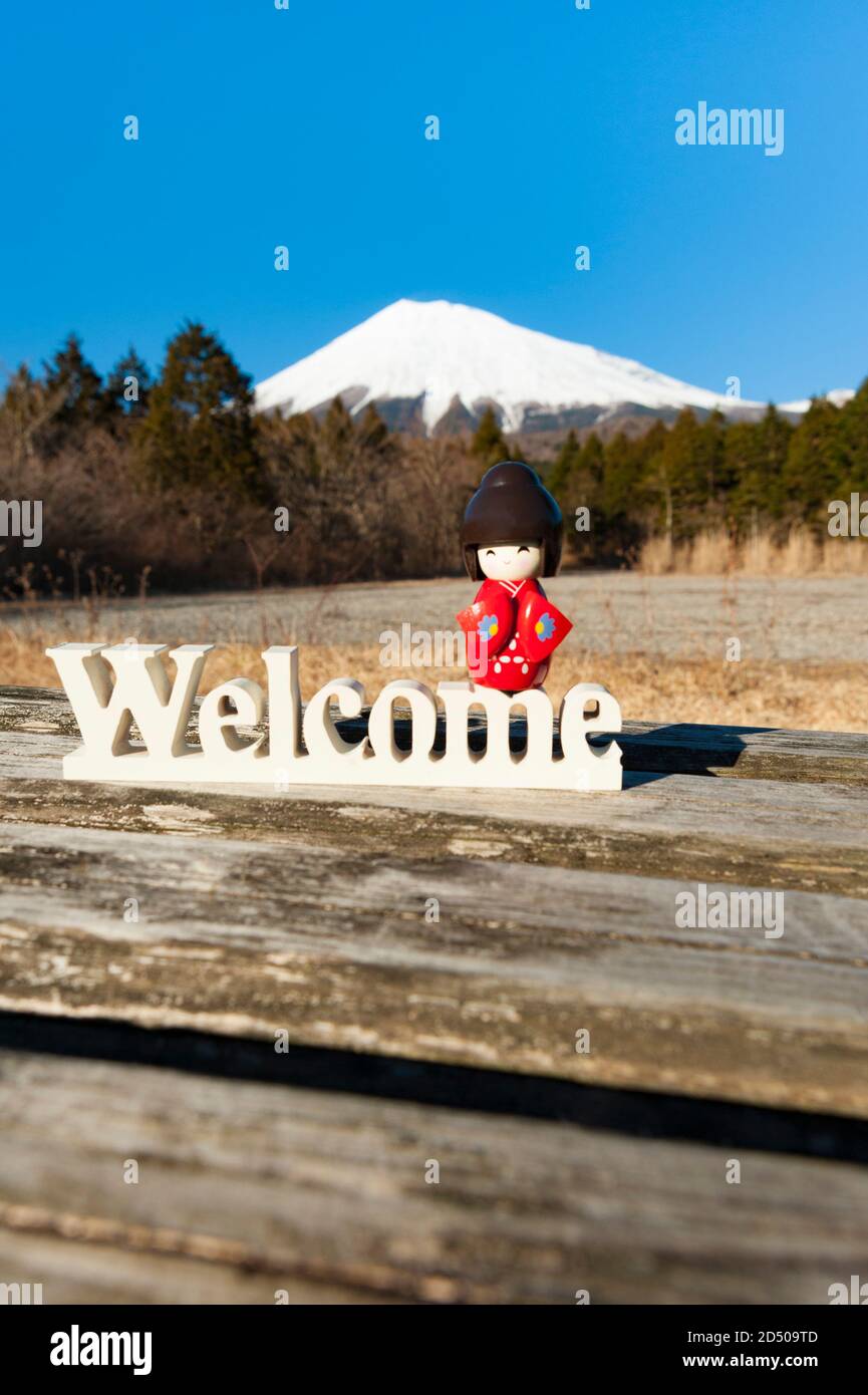 Magnifique poupée kokeshi traditionnelle japonaise vêtue de kimono rouge sur le mot 'Welcome'. Arrière-plan avec le Mont Fuji. Tir vertical. Banque D'Images