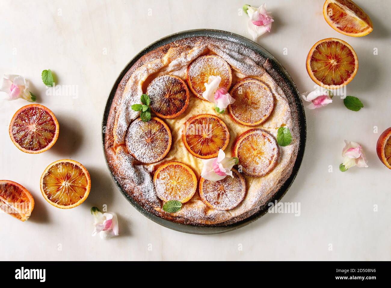 Gâteau au fromage fait maison avec des oranges sanguines de Sicile, décoré par des fleurs comestibles, les feuilles de menthe et le sucre en poudre a servi dans la plaque avec les oranges coupées au-dessus de o Banque D'Images