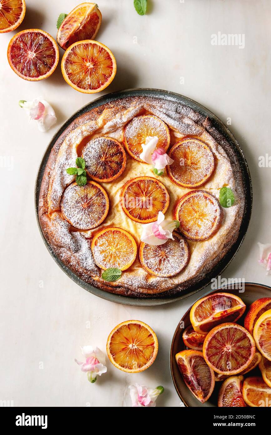 Gâteau au fromage fait maison avec des oranges sanguines de Sicile, décoré par des fleurs comestibles, les feuilles de menthe et le sucre en poudre a servi dans la plaque avec les oranges coupées au-dessus de o Banque D'Images