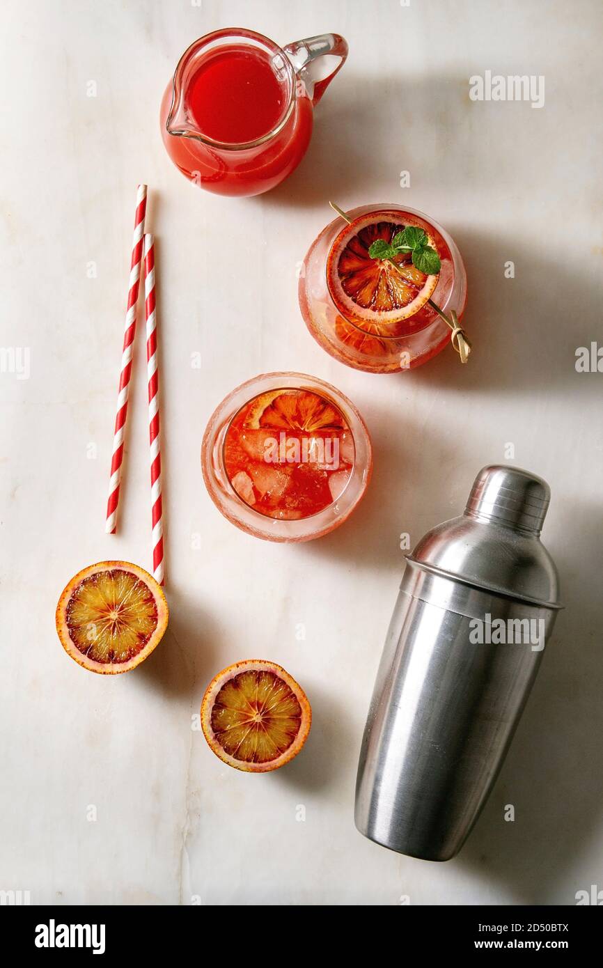 Cocktails glacés à l'orange de sang en verres, décorés de tranches d'oranges et de menthe fraîche sur brochettes, servis avec de la paille rétro, un pichet de jus et un shaker Banque D'Images