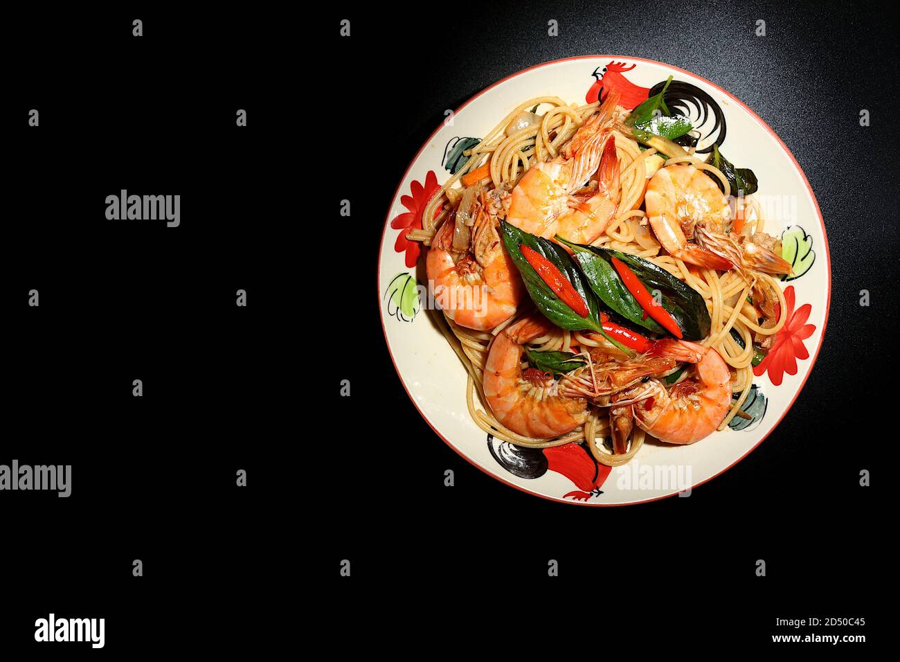 Remuez les spaghettis frits avec de la pâte de Chili, des crevettes, du basilic, du piment frais, des jeunes grains de poivre vert, de l'oignon, des carottes, des feuilles de caffir. Placez une plaque sur un bla Banque D'Images