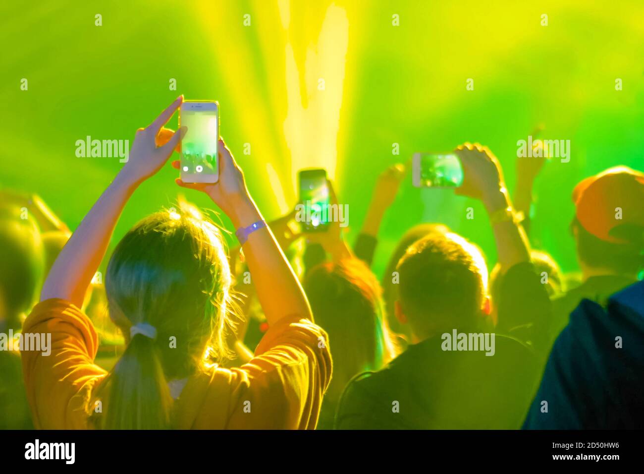 Adolescents prenant des photos ou enregistrant des vidéos de concert avec un smartphone - vue arrière. Éclairage de scène coloré et lumineux. Vie nocturne, technologie Banque D'Images