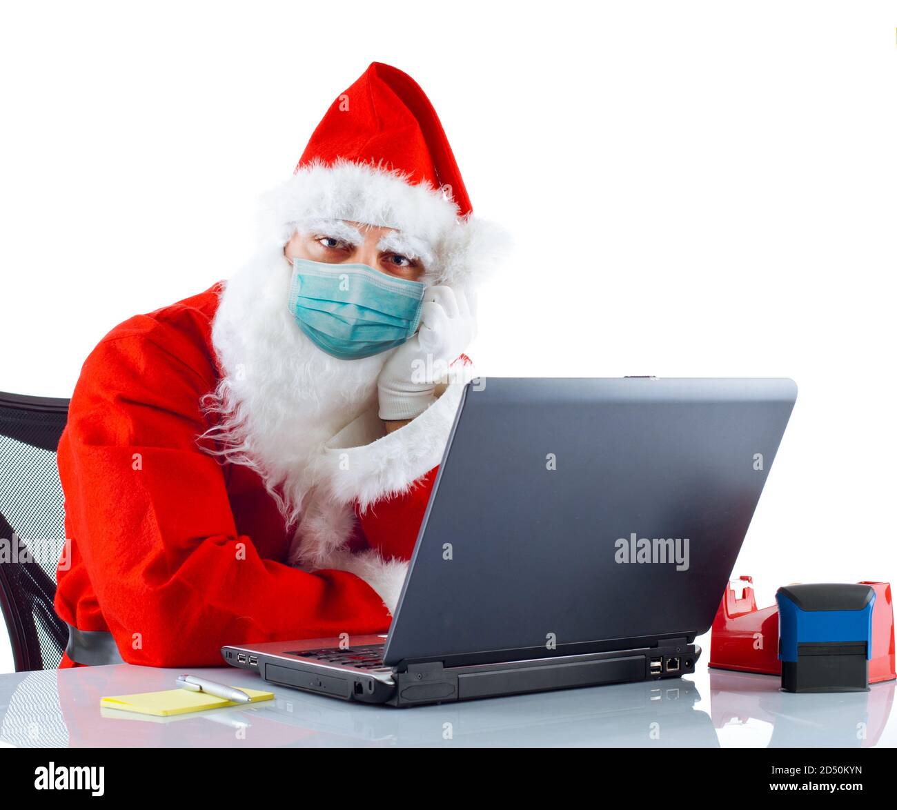 Le Père Noël avec masque chirurgical fonctionne avec un ordinateur portable sur fond blanc. Banque D'Images